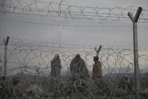 Migrants and refugees stand behind a fence reinforced with razor wire, on the border line with Greece near the southern Macedonia's town of Gevgelija, Monday, Feb. 29, 2016. More than 6000 migrants and refugees are stuck in the border after neighbor Macedonia began slowing the number of crossings heading to central and northern Europe. (AP Photo/Petros Giannakouris)